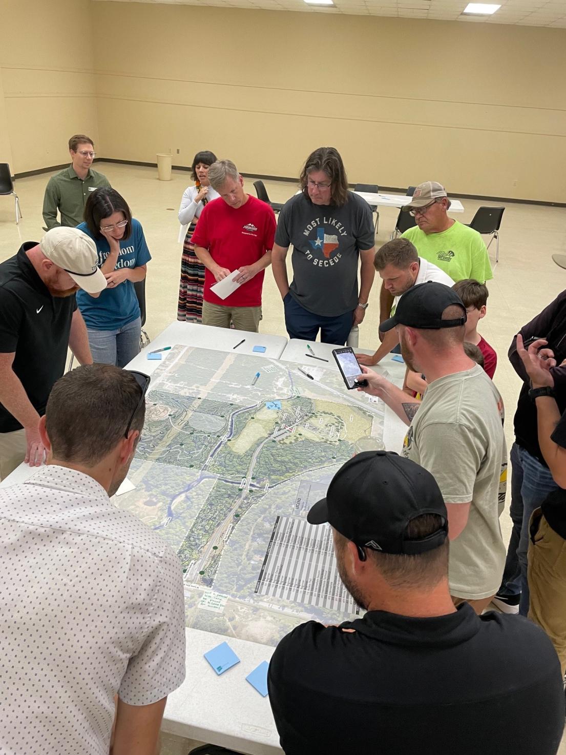 Committee members stand around large park map placing notes during planning meeting