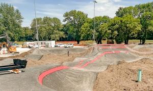 Bicycle pump track with red lines winding through a park, surrounded by trees.