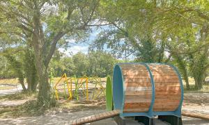 Playground with tunnel, surrounded by trees and sunny skies.